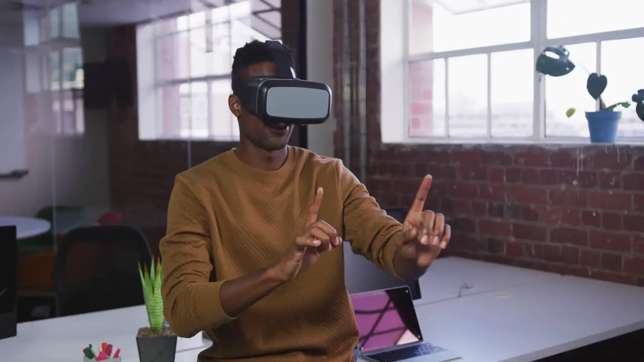 African american businessman sitting on desk using vr headset and gesturing