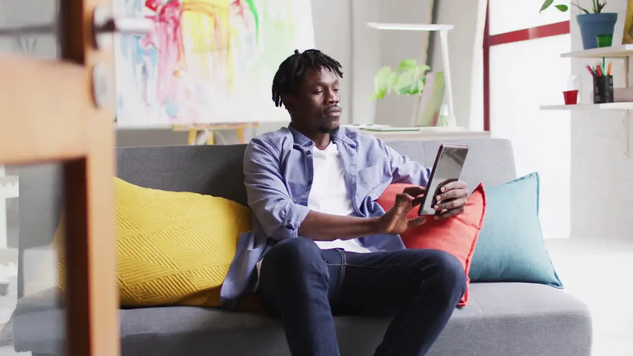 African american male artist using digital tablet while sitting on the couch at art studio