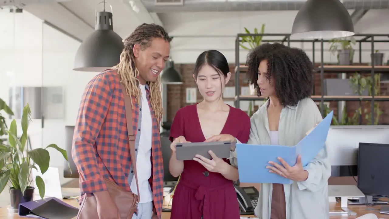 Portrait of happy diverse casual colleagues with tablet discussing in creative office in slow motion