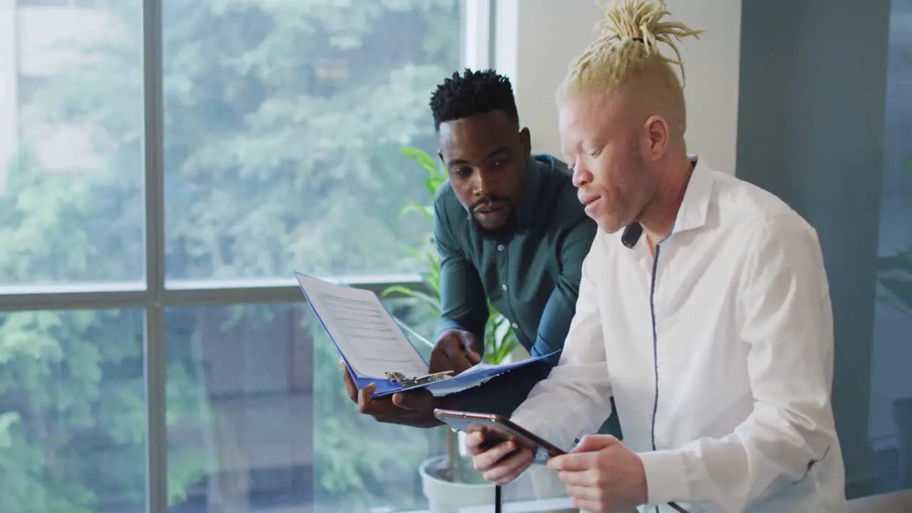 Diverse businessmen discussing with documents and tablet in creative office