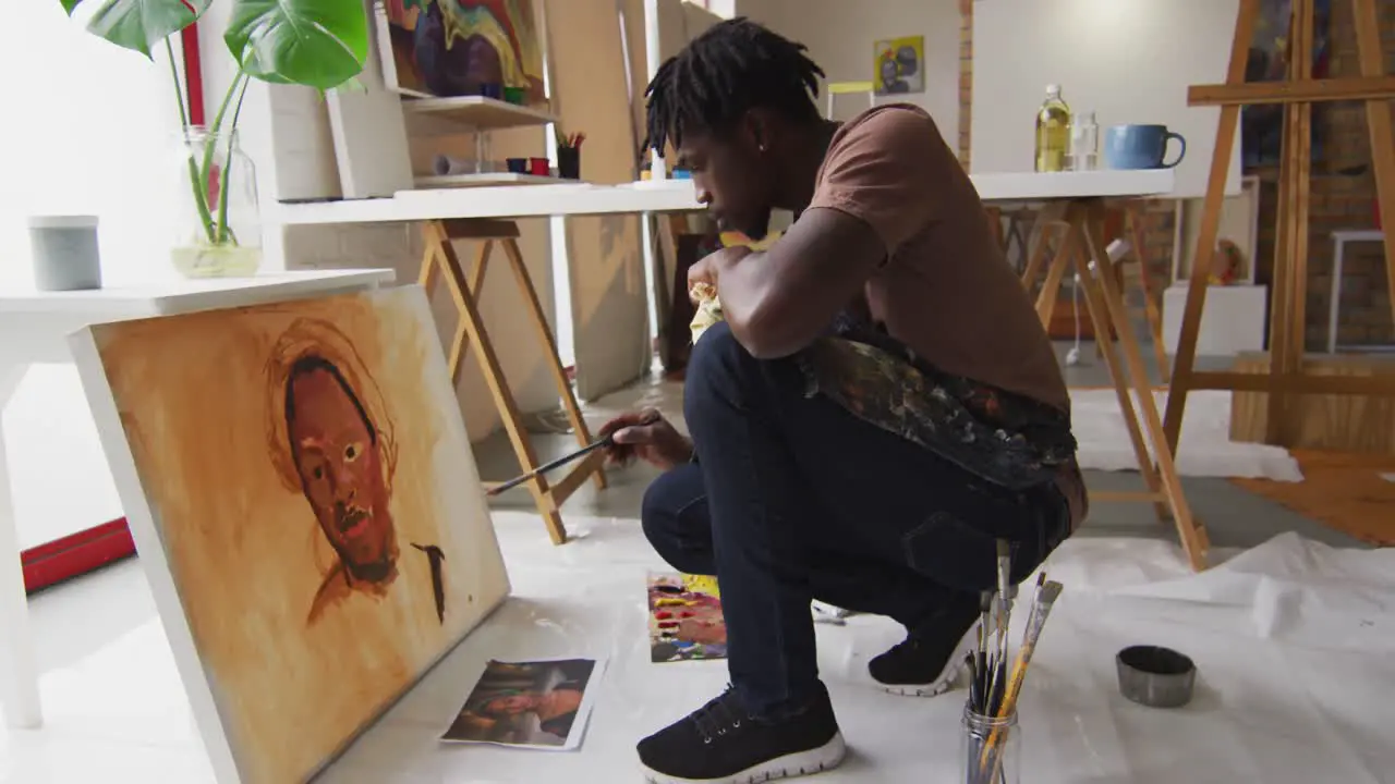 Side view of african american male artist wearing apron painting on canvas at art studio