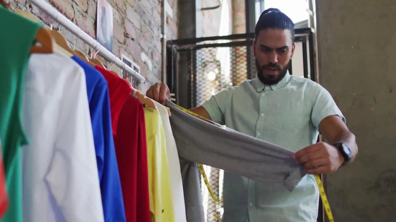 Mixed race male fashion designer looking at different clothes and smiling