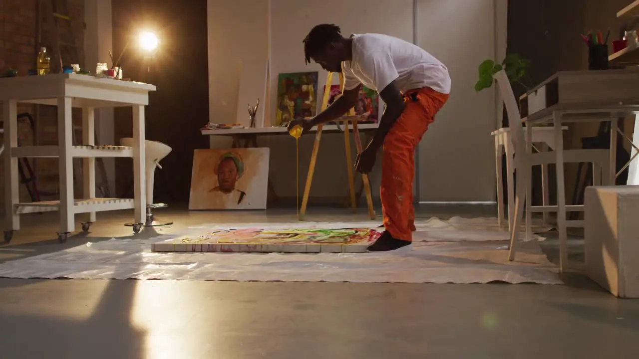 African american male artist pouring paint on canvas and painting at art studio