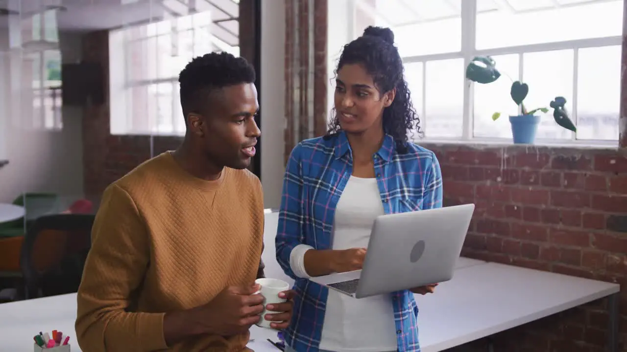 Diverse female and male business colleagues in discussion at work looking at laptop