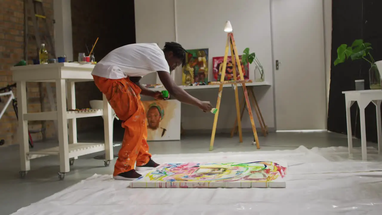 African american male artist pouring paint with a paint brush on canvas at art studio