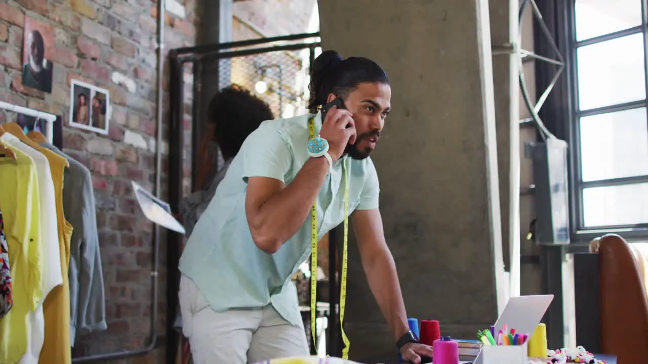 Diverse male and female fashion designers talking on smartphone and hanging pictures