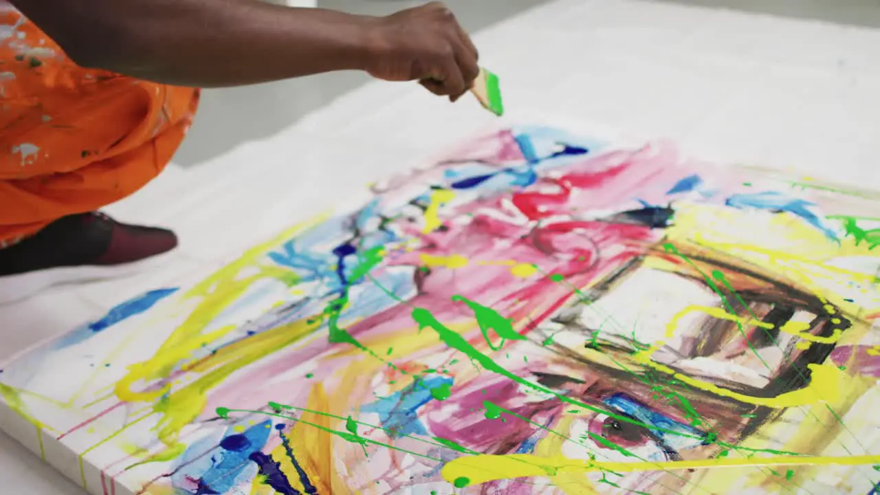 Close up of african american male artist pouring paint with a paint brush on canvas at art studio