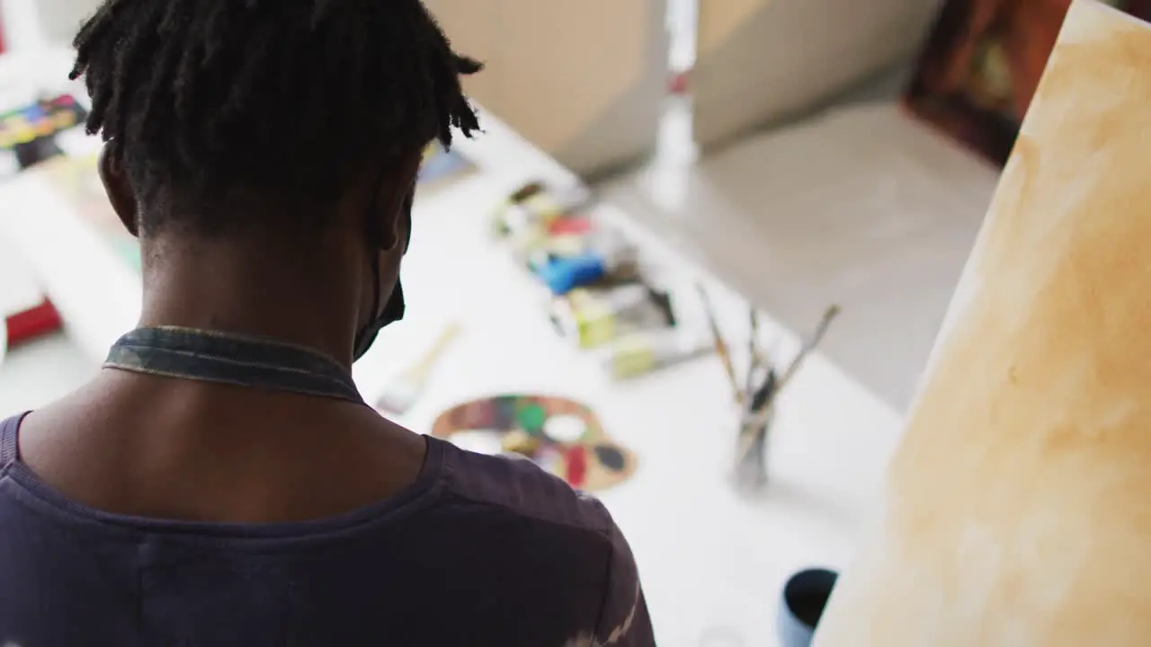 Rear view of african american male artist mixing colors in the palette with a brush at art studio