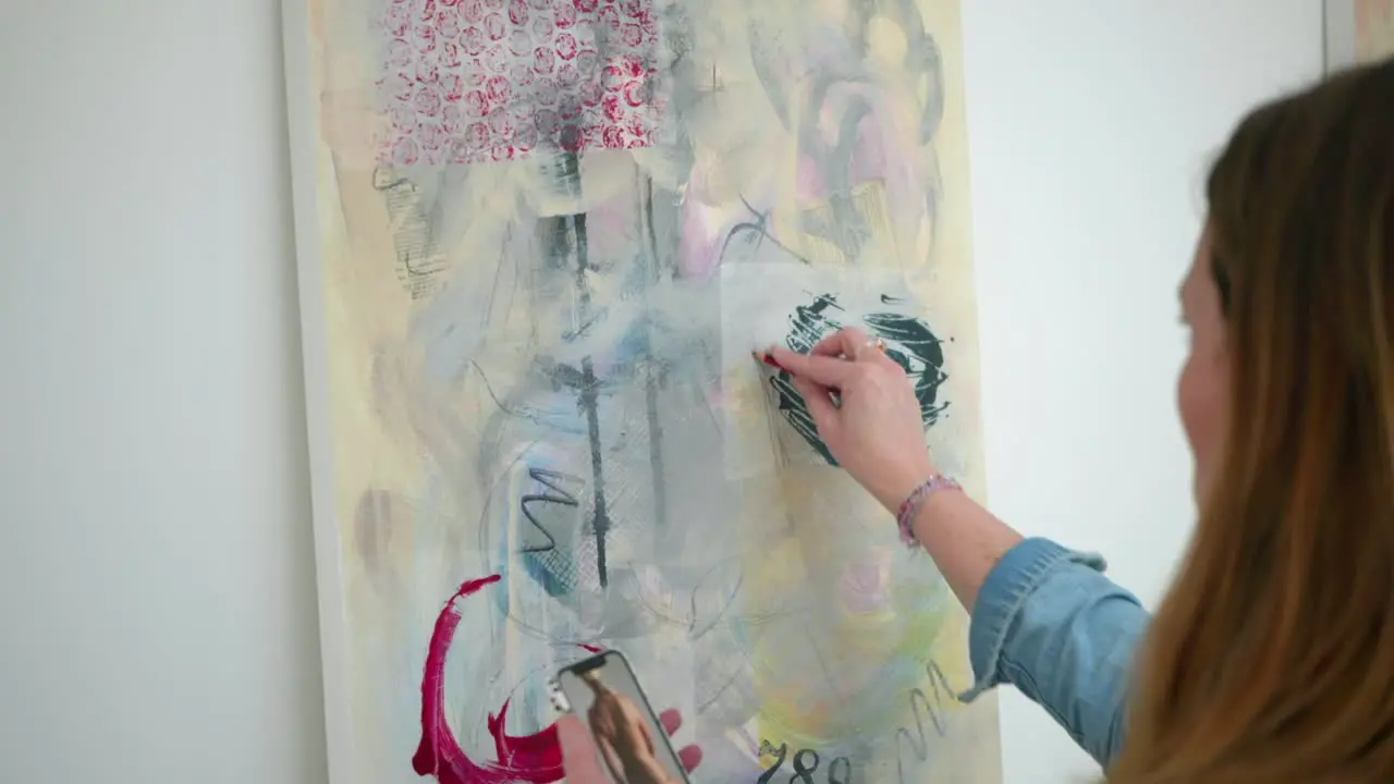 Female artist checks composition of painting on canvas with fingers and pencil