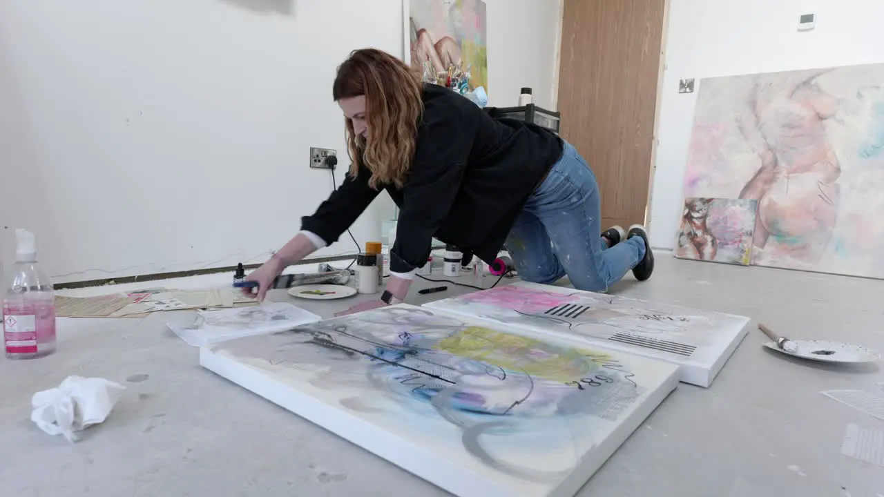 Female artist on floor of a busy home studio preparing to paint a canvas