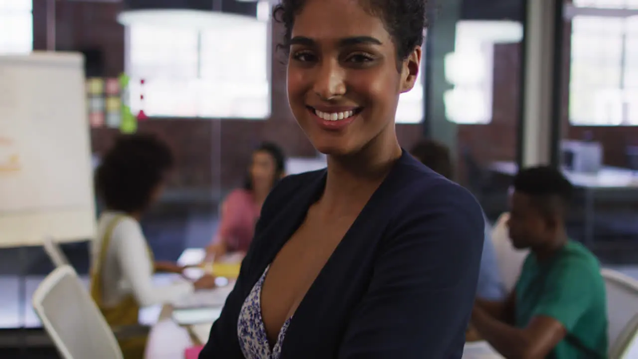 Happy mixed race businesswoman standing and smiling with colleagues in background