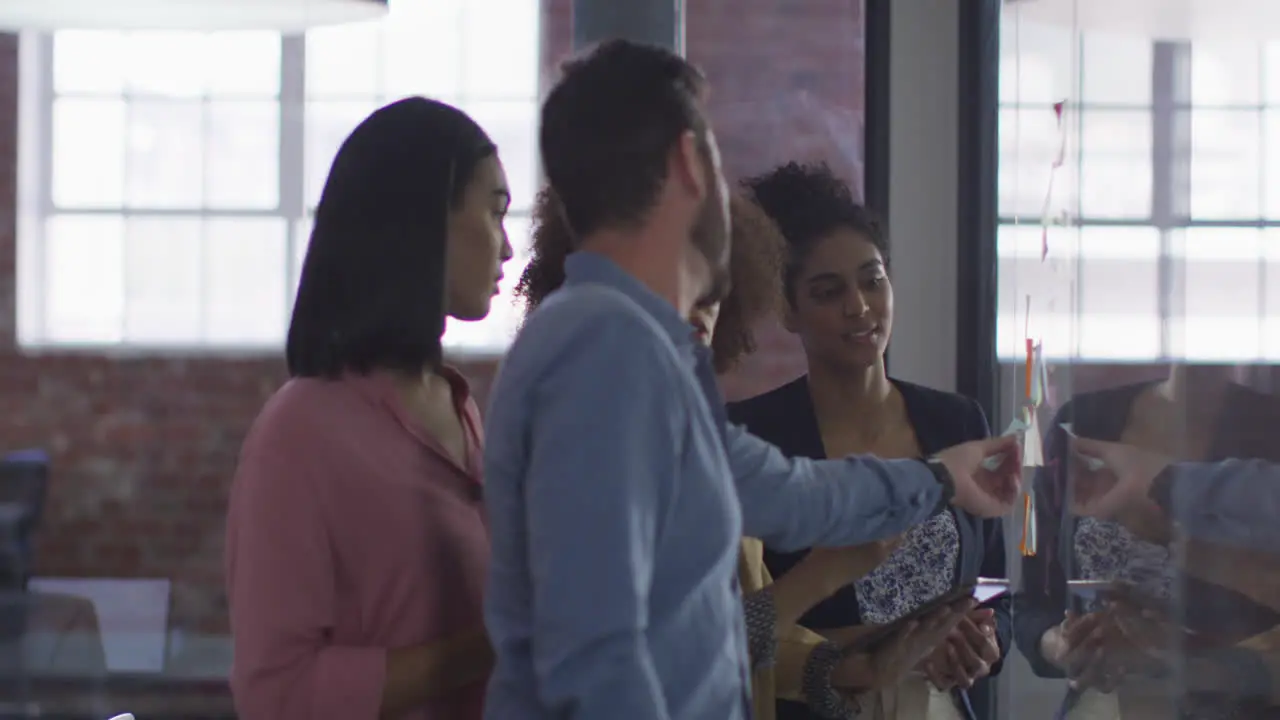 Diverse colleagues using memo notes on glass wall having a discussion