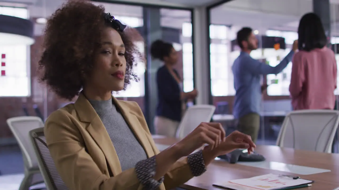 Mixed race businesswoman sitting smiling in meeting room with diverse colleagues in background