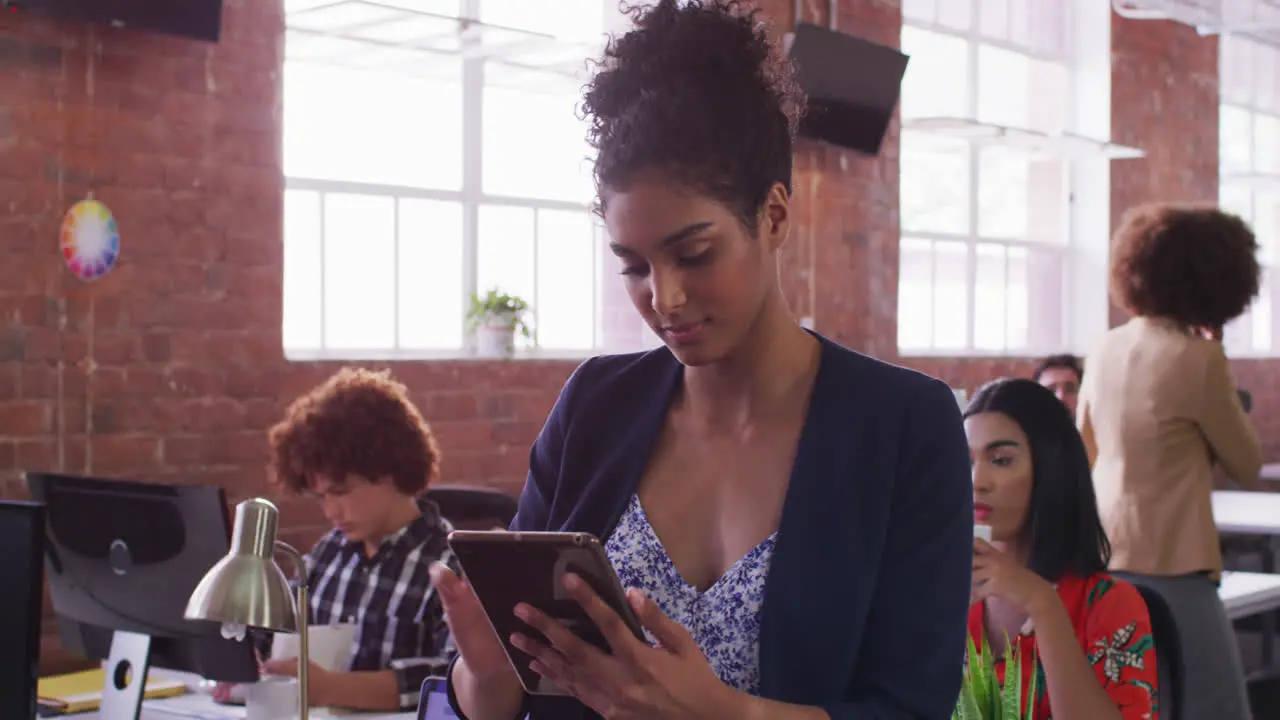 Mixed race businesswoman using tablet in office with diverse colleagues in background