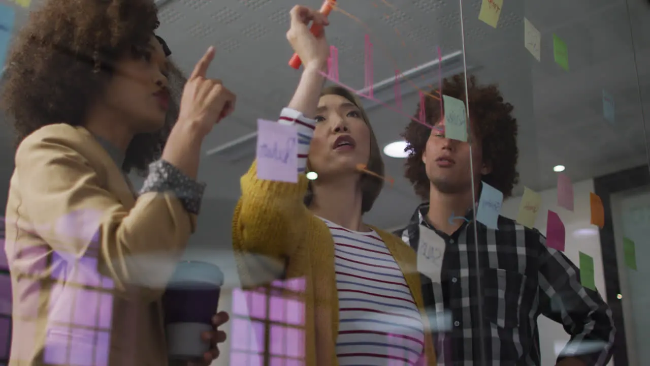 Diverse work colleagues using memo notes and writing on glass wall having a discussion