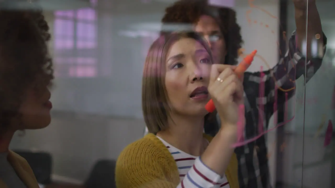 Diverse work colleagues writing and drawing on glass wall having a discussion