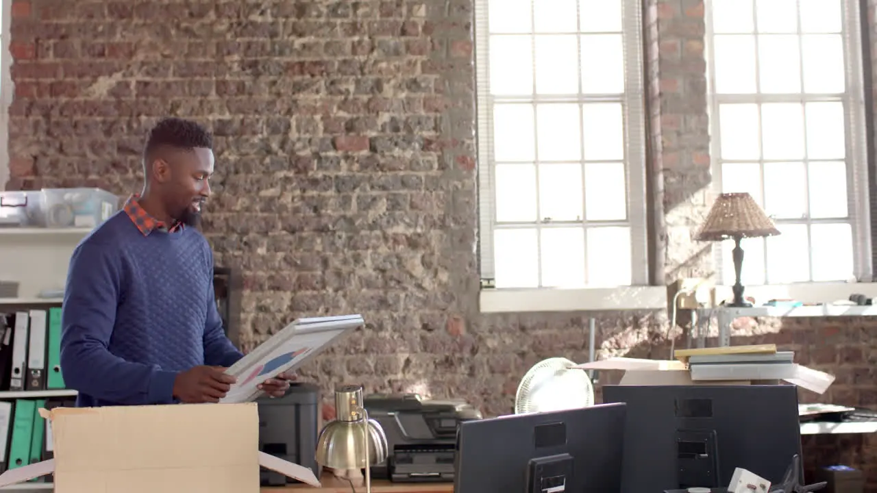 Happy african american casual businessman holding images in creative office in slow motion