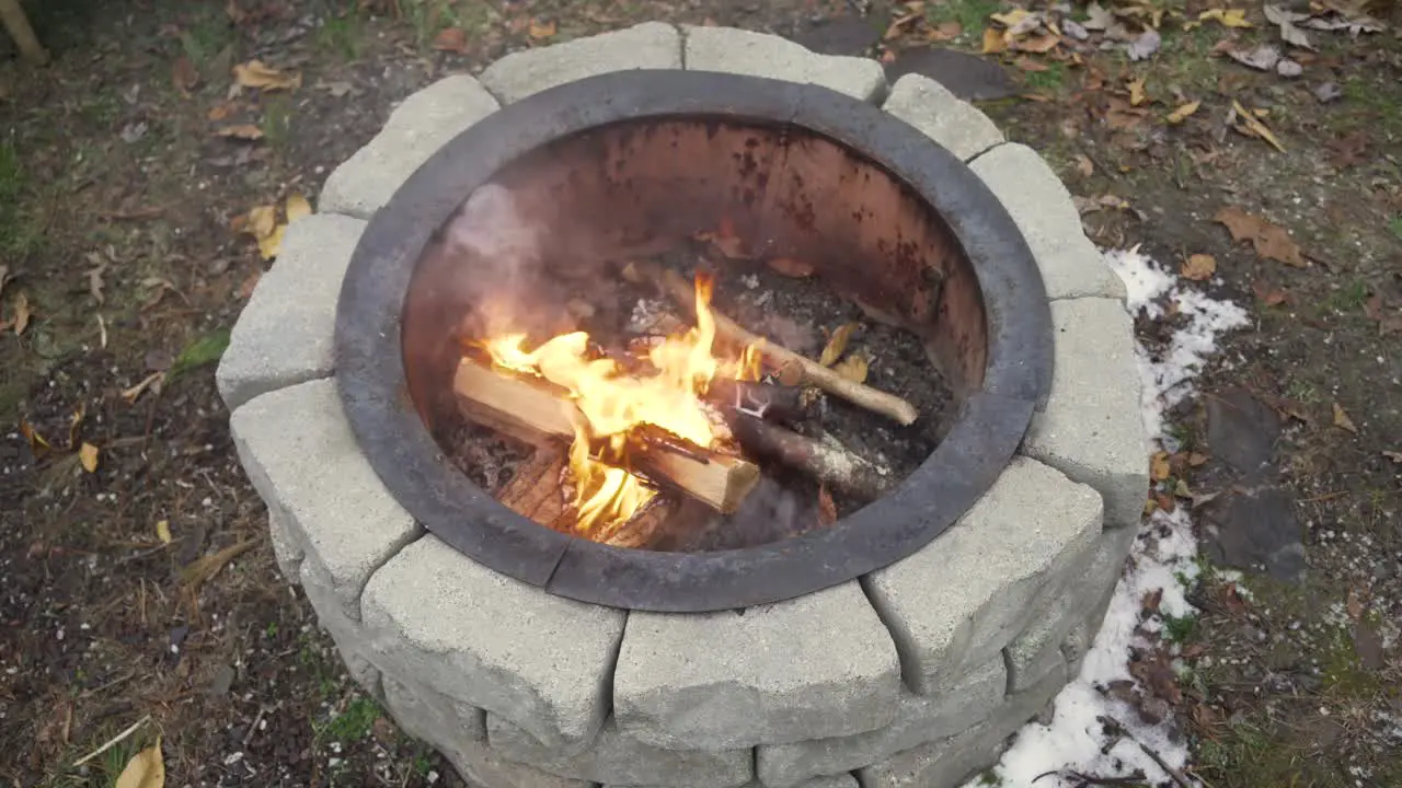 Wide top view of fire burning in a fire pit with snow and leafs on the ground