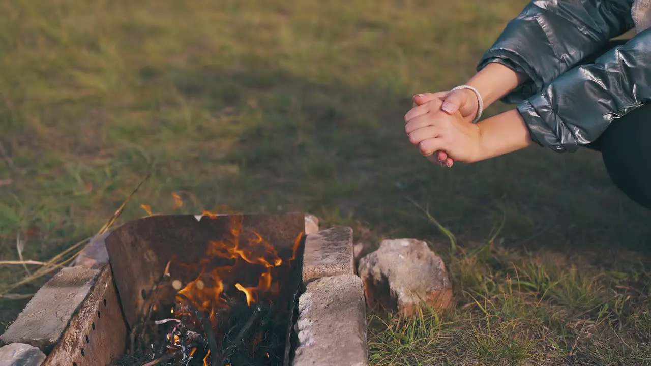 girl hiker heats hands at burning bonfire at camp closeup