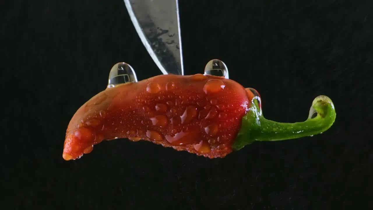 Close Up Rotating Zoom on a Wet Red Chili Pepper on the Tip of a Knife in front of a Black Background