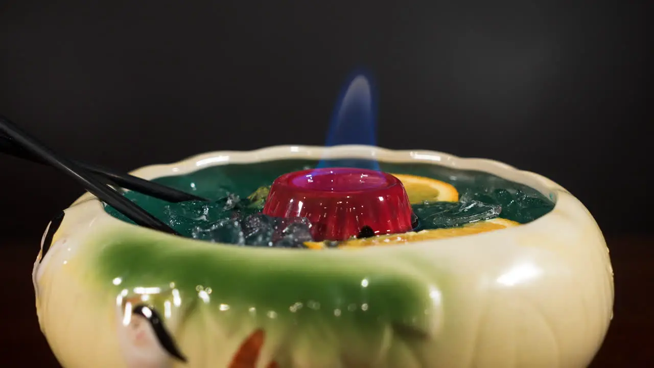 Tropical tiki style cocktail in large bowl with orange slices burning flame sake punch beverage slider close up 4K