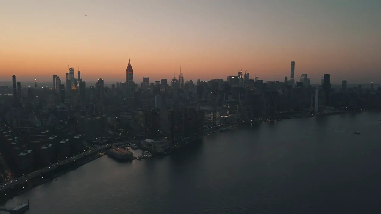 AERIAL Over East River showing Manhattan New York City Skyline in Beautiful Dawn Sunset Orange Light right before Dark