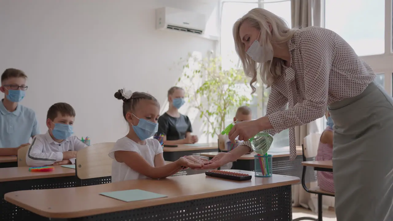 The teacher treats the hands of an antiseptic girl in the classroom at school before class coronavirus and the pandemic at school The work of the school in the epidemic mode