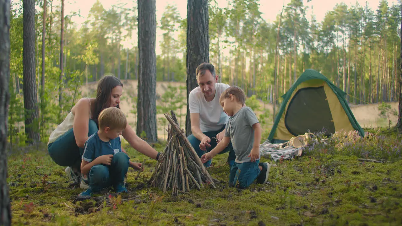 Family sits around a campfire on a summer evening Children with their parents are resting in the woods Weekend in nature in good company Family frying sausages over a fire in the woods