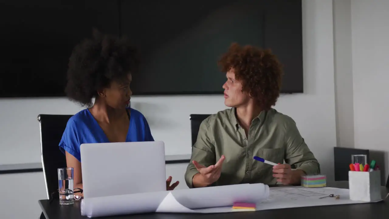 Diverse male and female business colleagues in discussion at work using laptop computer