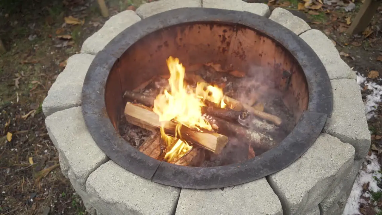 Top view of fire burning in a round stone pit with small amounts of snow around