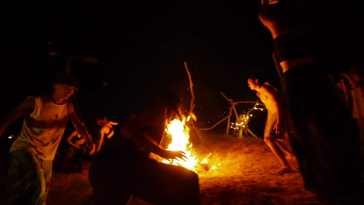 Group of Asian dancers rotating around flaming hot ceremonial fire during night time dance performance filmed hand held as wide shot