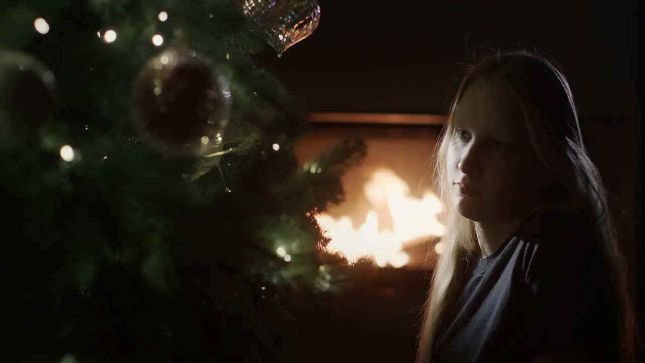 Girl is sitting in the dark near a Christmas tree in the background a fire is burning in a fireplace Christmas Eve