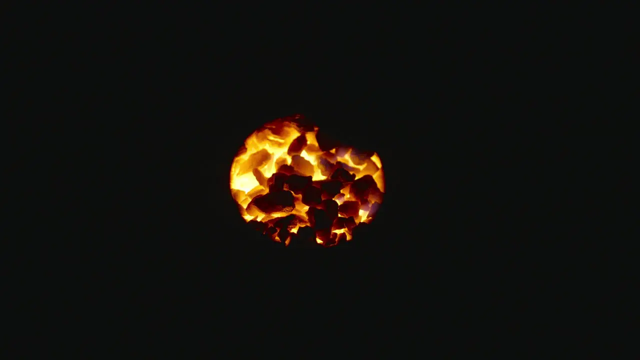 Coals of fire glowing in the dark through a hole close up shot