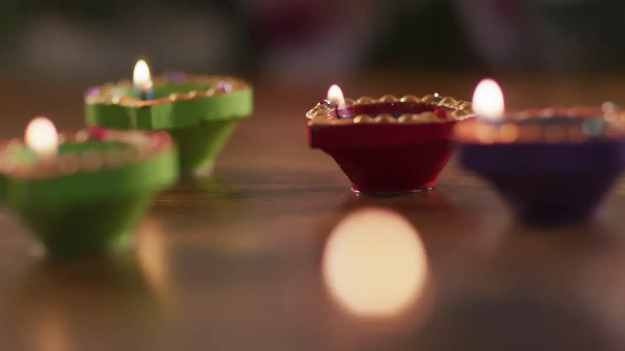 Four lit candles in decorative clay pots on wooden table top bokeh flame in foreground