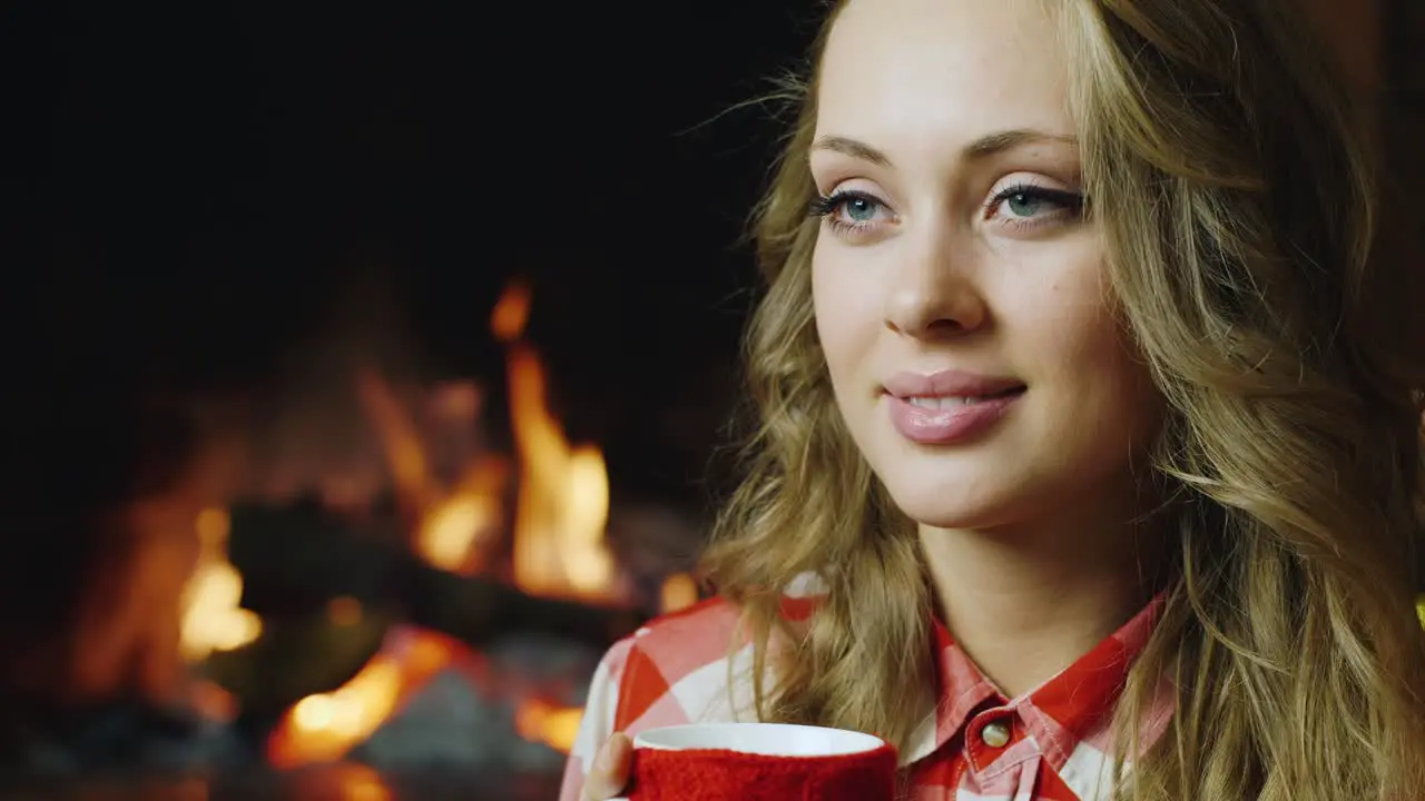 A young woman drinks tea by the burning fireplace