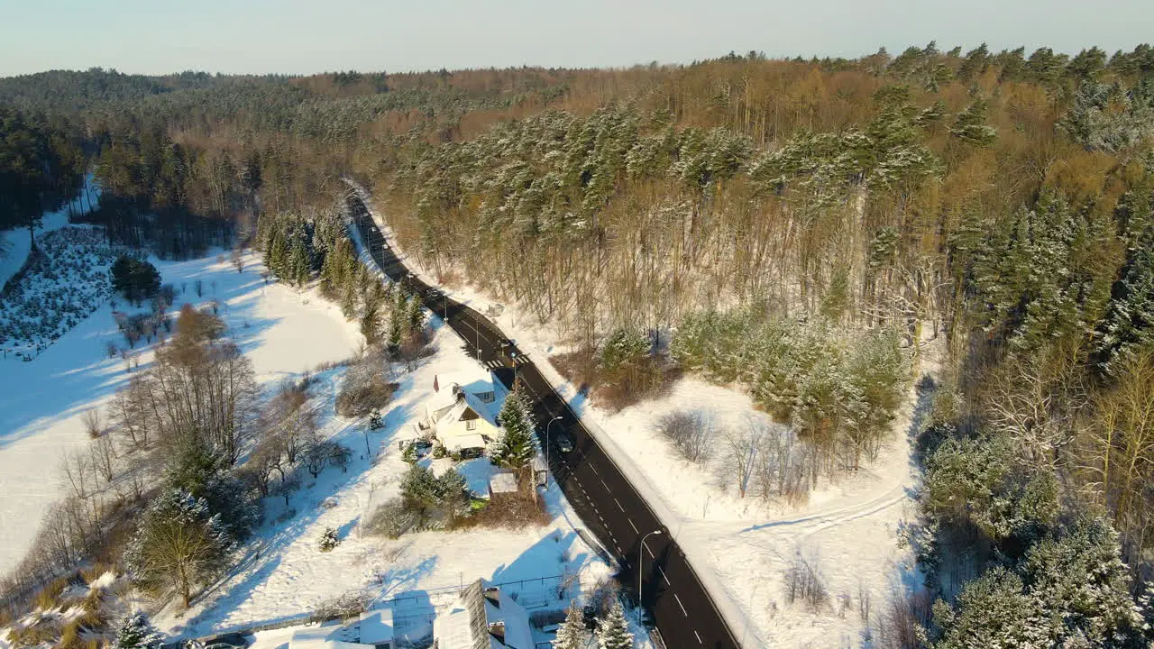 Cars driving in opposite directions on a black asphalt road with the side of the road covered with white snow between a streched green winter forest