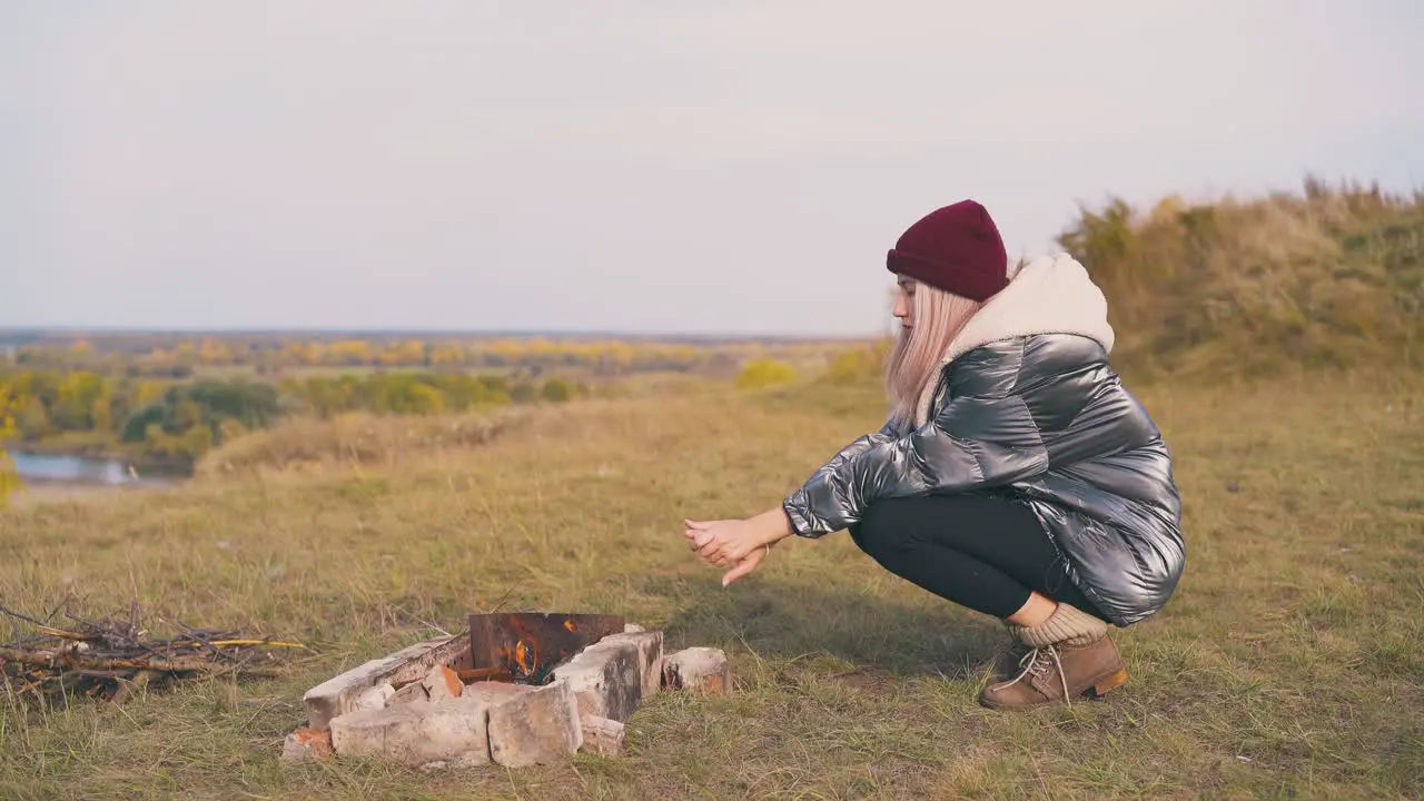 pretty woman heats palms at bonfire on meadow in camp