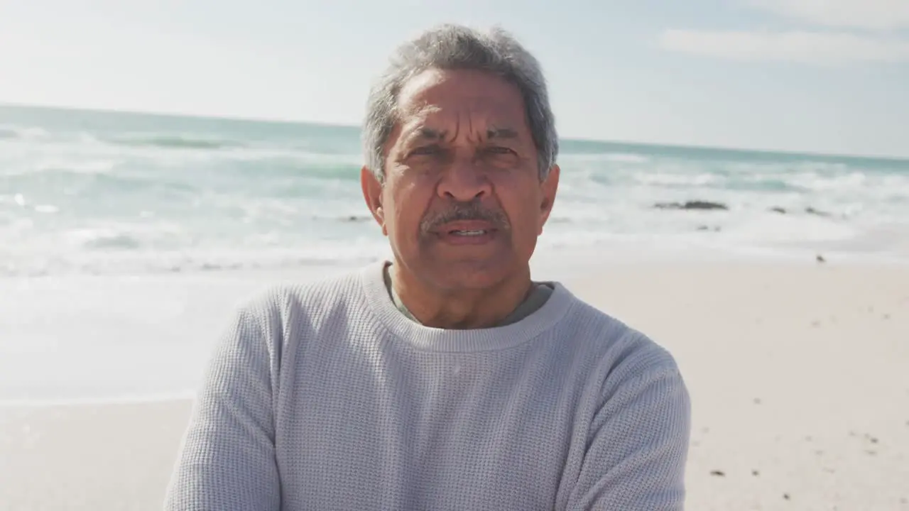 Portrait of hispanic senior man standing on beach and looking at camera