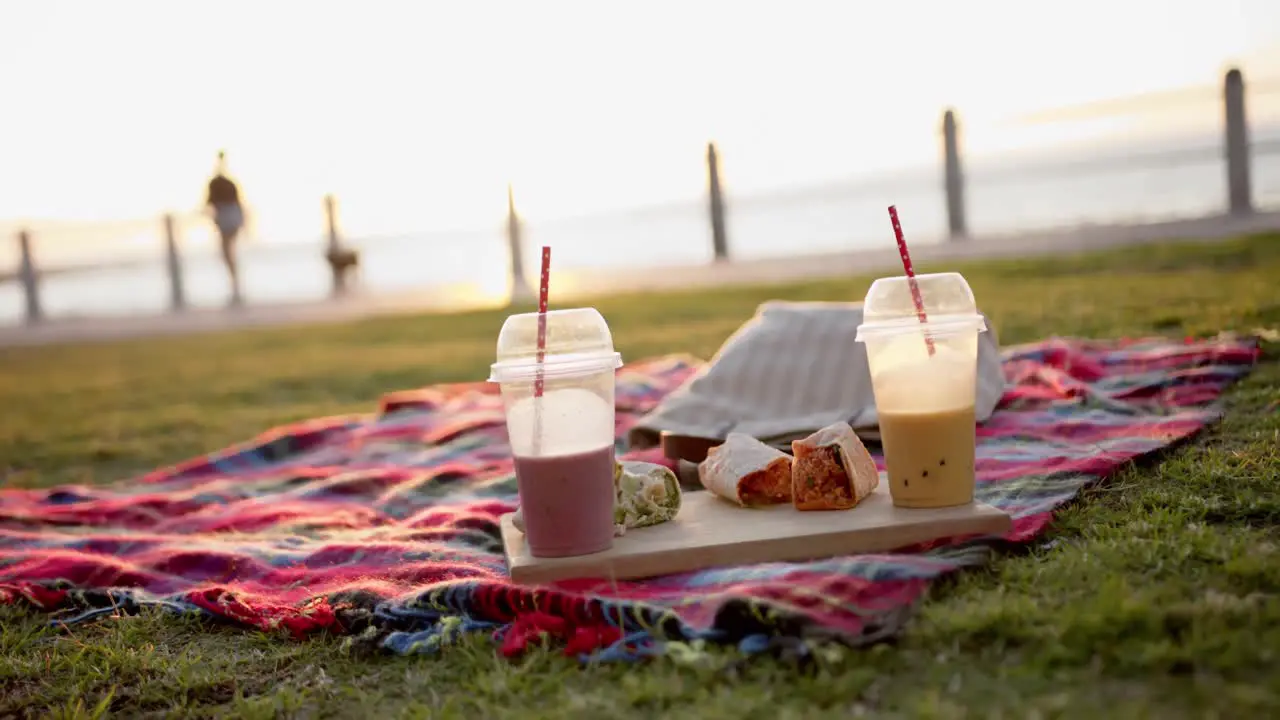 Close up of blanket with smoothies and tortillas at picnic on promenade by the sea slow motion