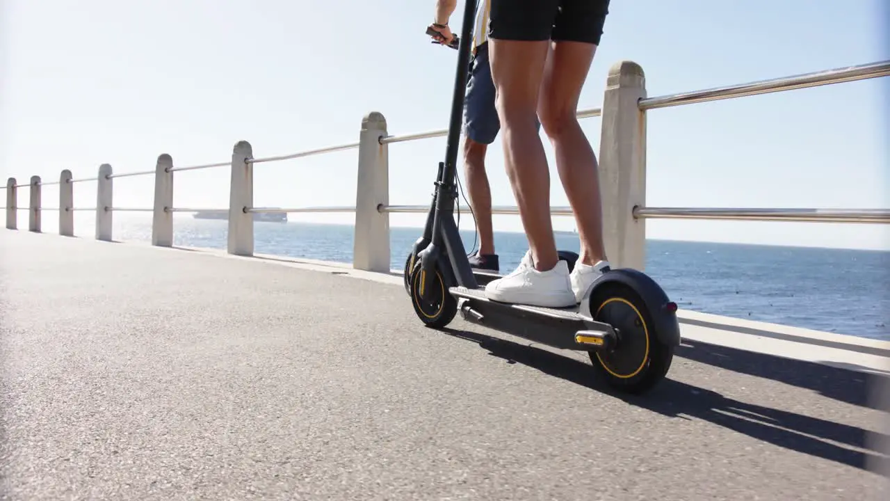 Midsection of diverse gay male couple using scooters at promenade by the sea slow motion