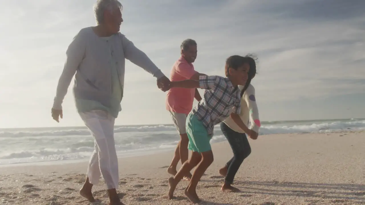 Happy hispanic grandparents and grandchildren running on beach at sunset