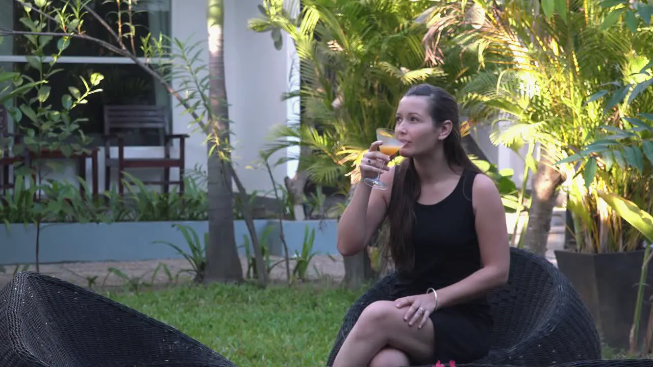 Medium Shot of a Beautiful Young Lady Playing with a Flower While Enjoying a Cocktail in the Tropical Hotel Grounds