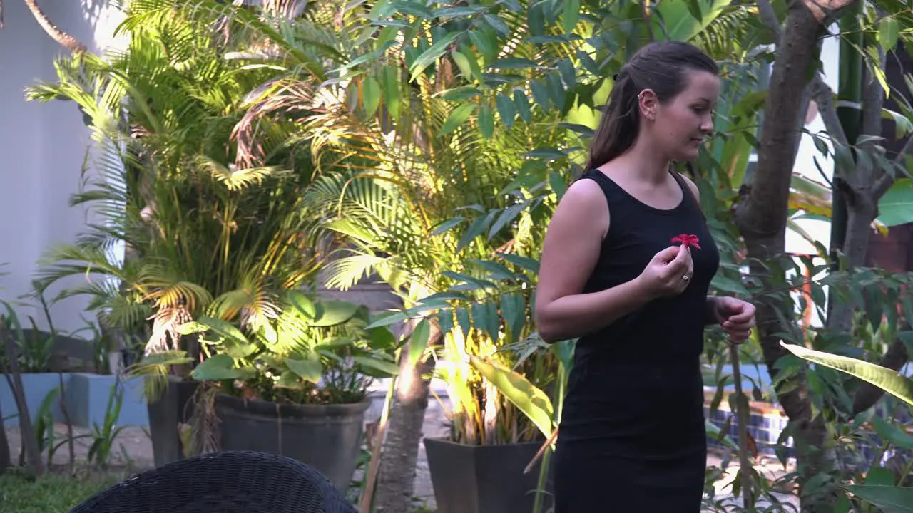 Medium Shot of a Beautiful Young Lady Playing with a Flower While Exploring the Tropical Hotel Grounds