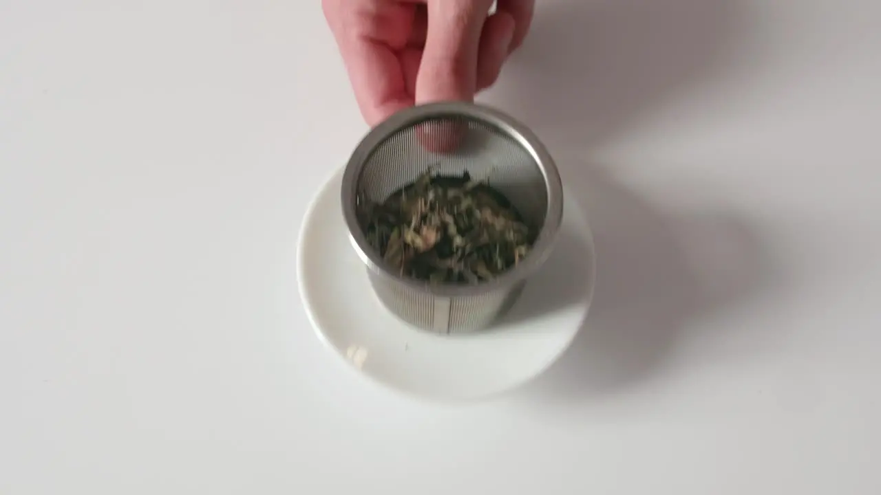 Bulk tea leaves in a metal tea filter being picked up