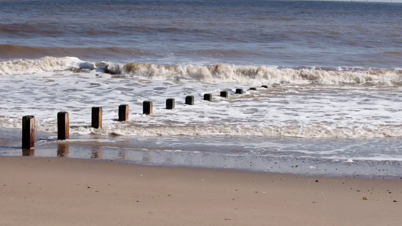 Waves crashing in to groynes on Skegness beach wide shot