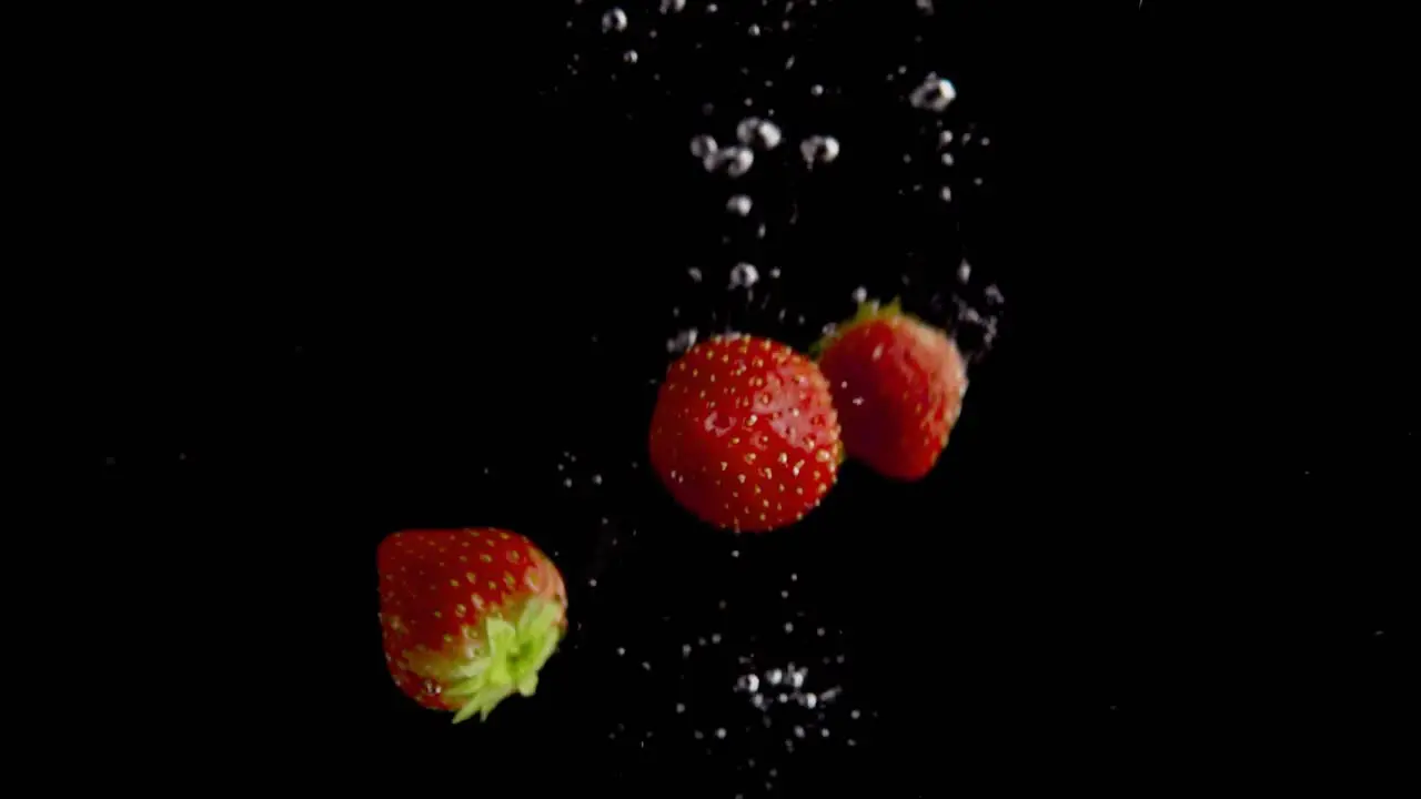 Strawberries Falling into Water Super Slowmotion Black Background lots of Air Bubbles 4k240fps