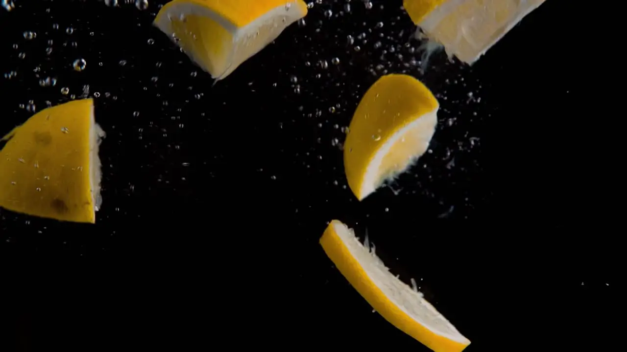 Lemon Pieces and Slices Falling into Water Super Slowmotion Black Background lots of Air Bubbles 4k240fps