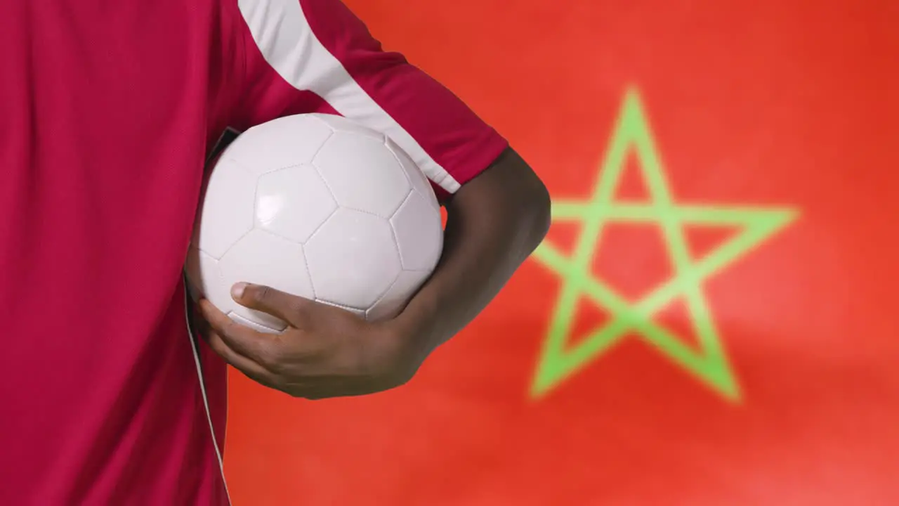 Young Footballer Walking Holding Football In Front of Morocco Flag