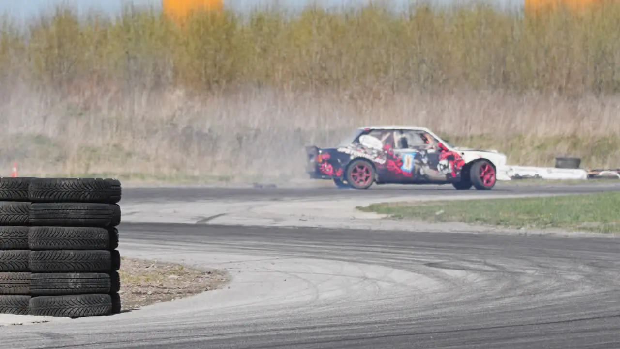 Slow motion shot of a drifting car on a race track with a pile of tires and s turn