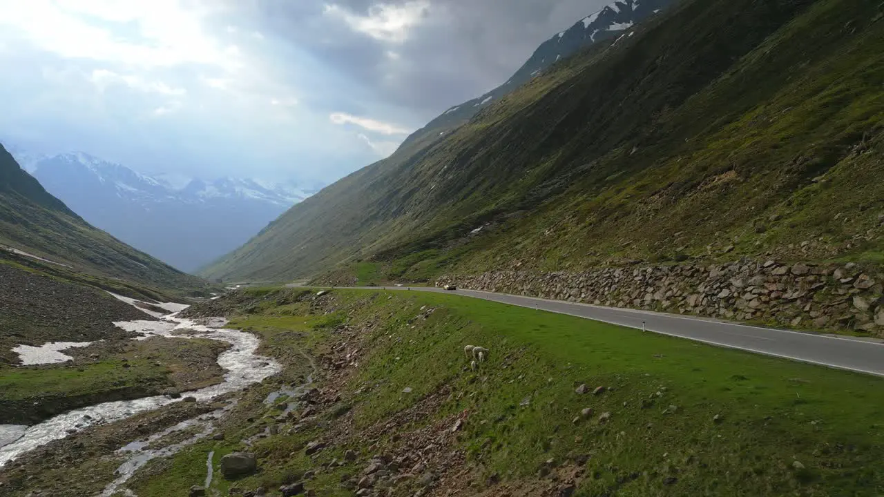 Close cinematic drone shot of a single car through a mountain road in the alps